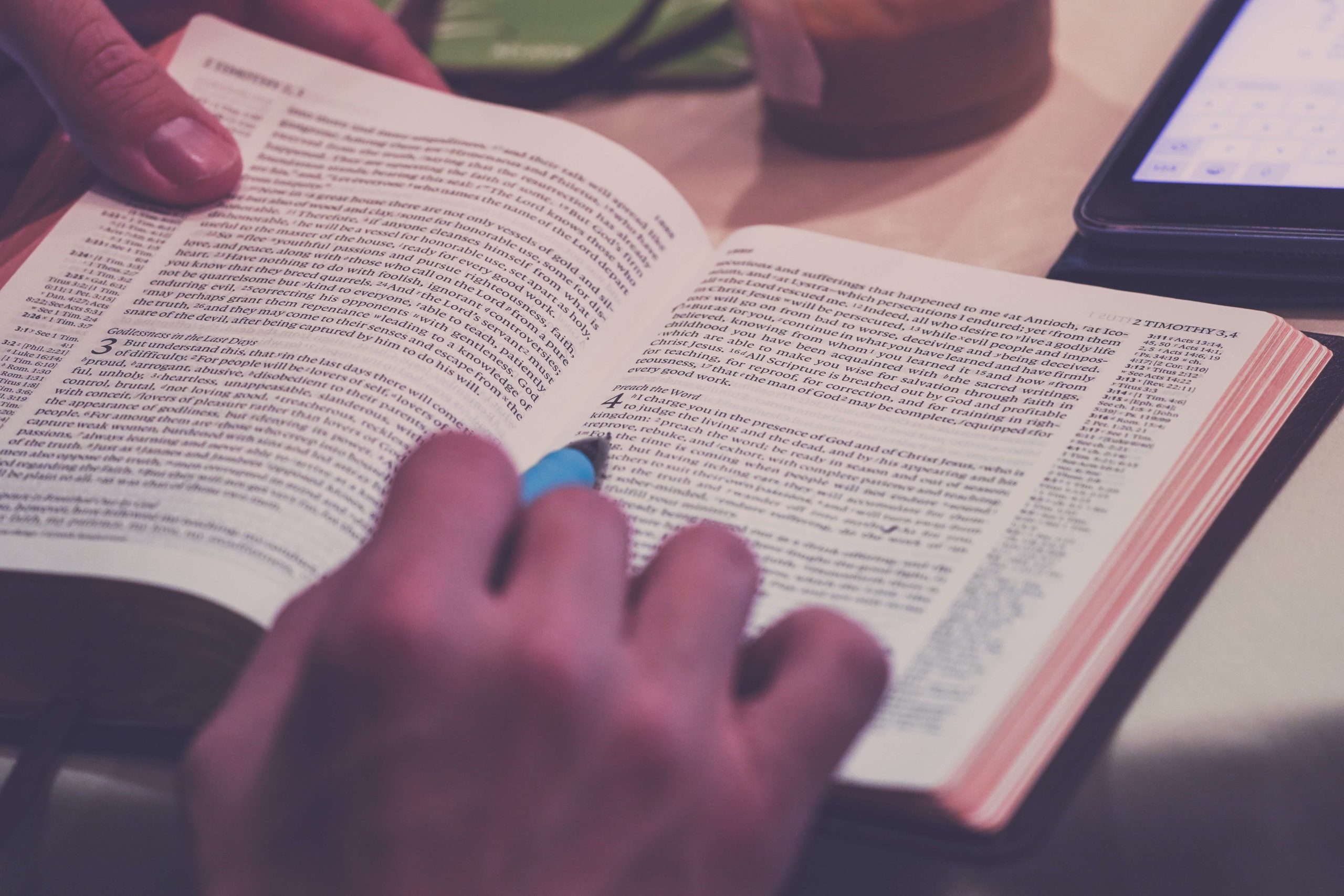open bible with a hand holding pen
