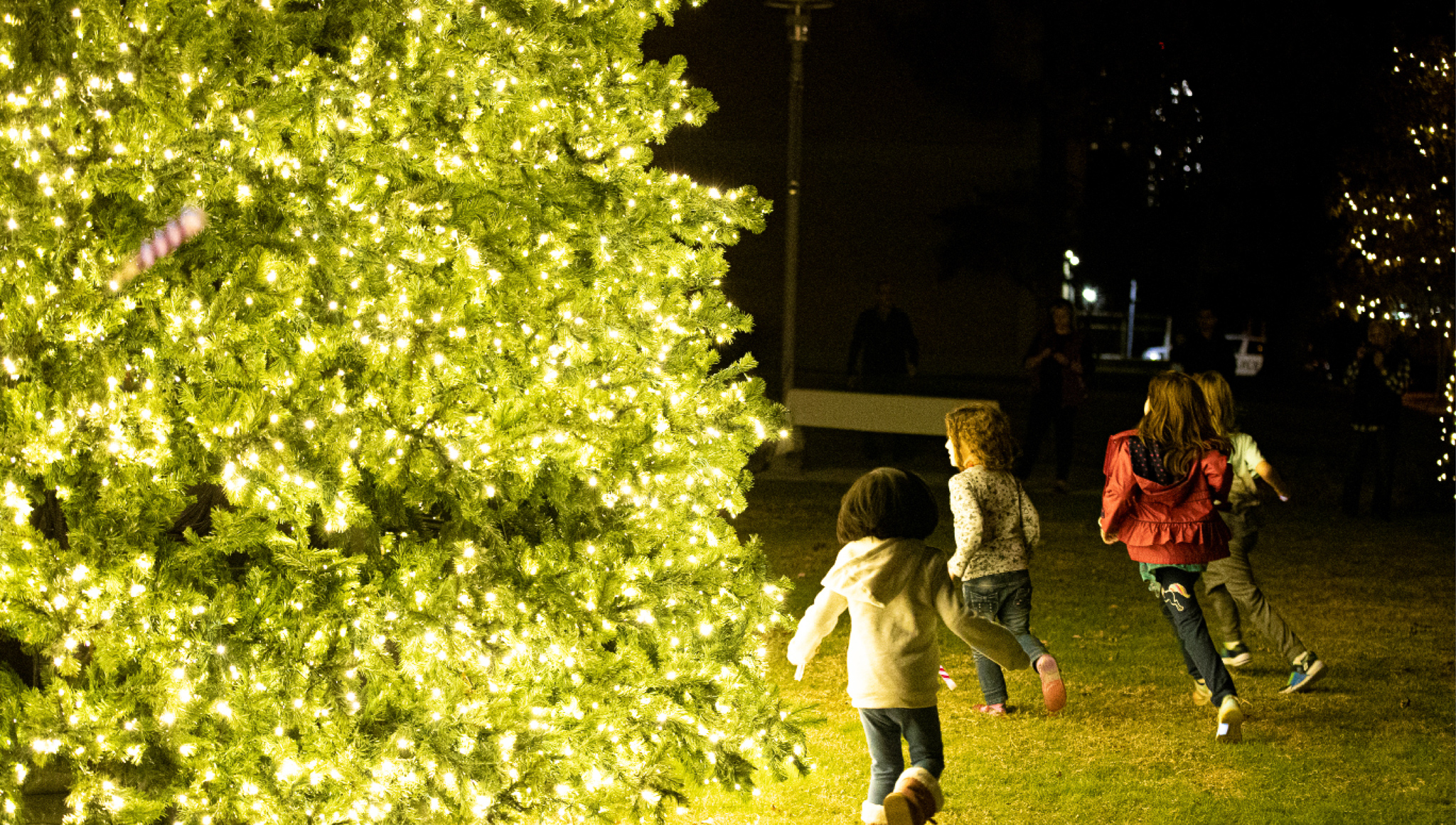 kids running around lit Christmas tree